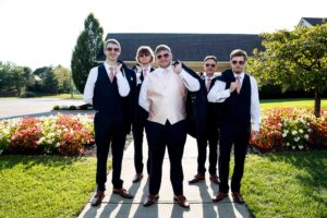 a groom's man group of guys standing "cool" with sunglasses and jackets flung over their shoulders. The groom stands out in a different color, pink, vest. This photo is meant to let grooms know they can share my wedding photography with their grooms men.
